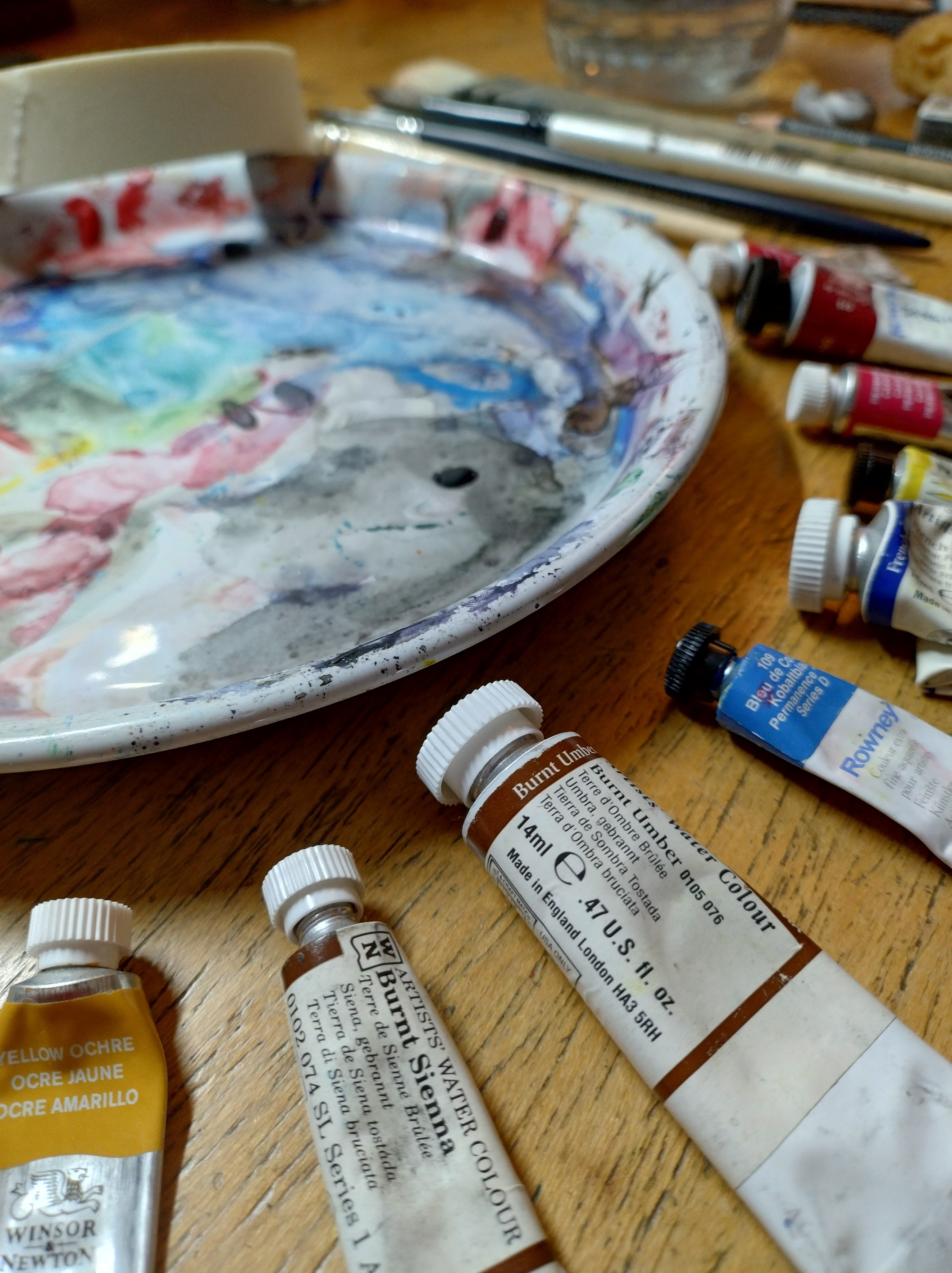 A white plate for a watercolour palette and some tubes of paint.